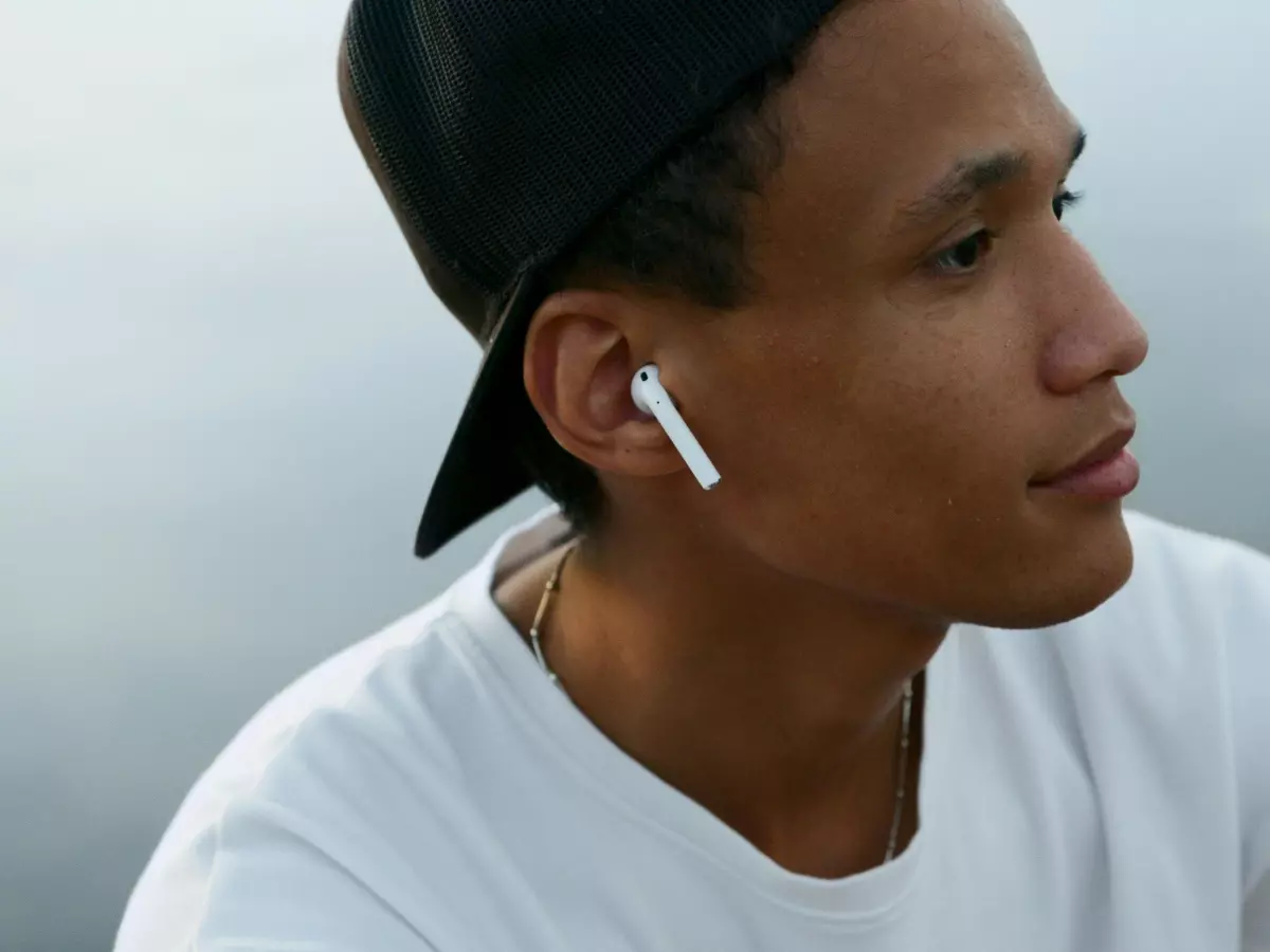 A person wearing white earphones is looking away thoughtfully.