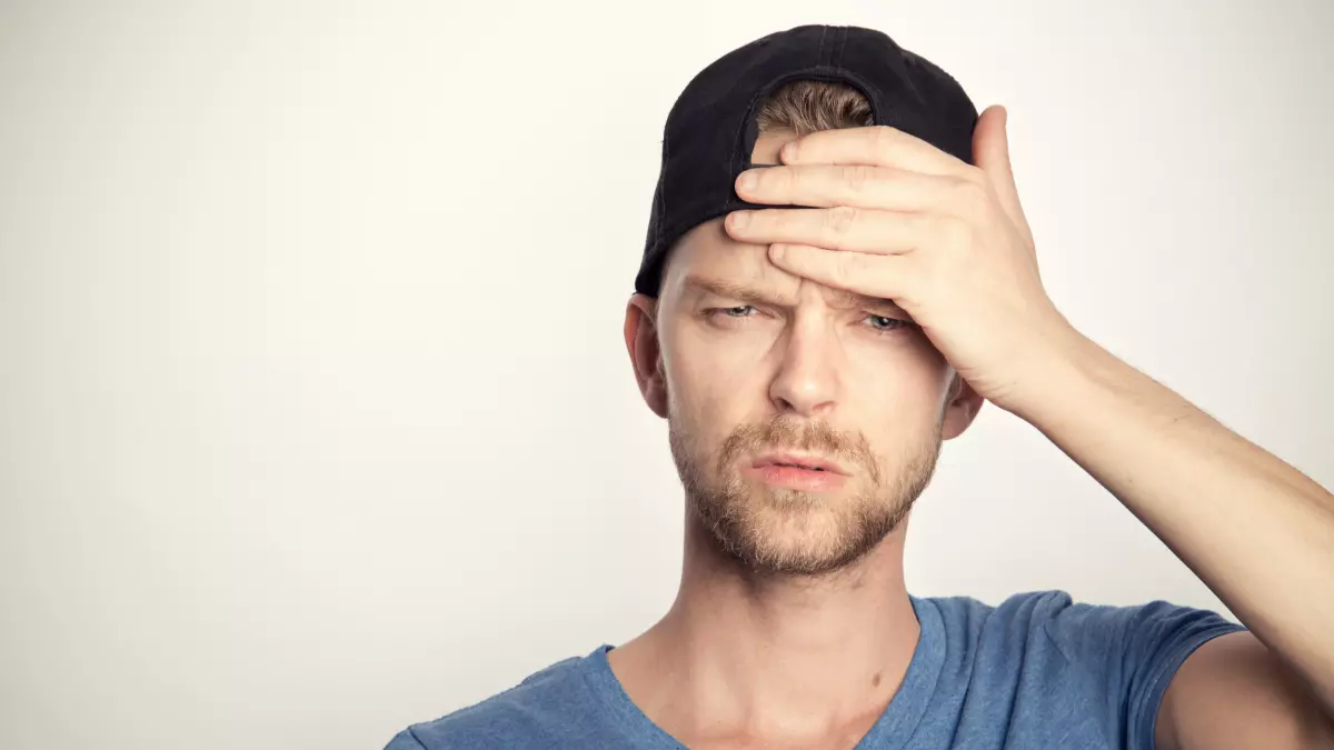 A man with a black cap, is looking stressed with his hand on his forehead