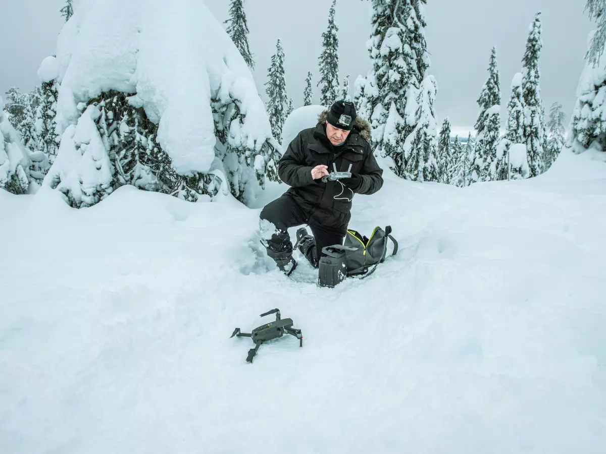 A man is sitting in the snow and controlling a drone