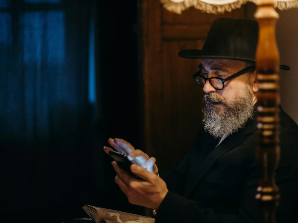 An older man in a hat and glasses is using an iPhone in a dim lit room.