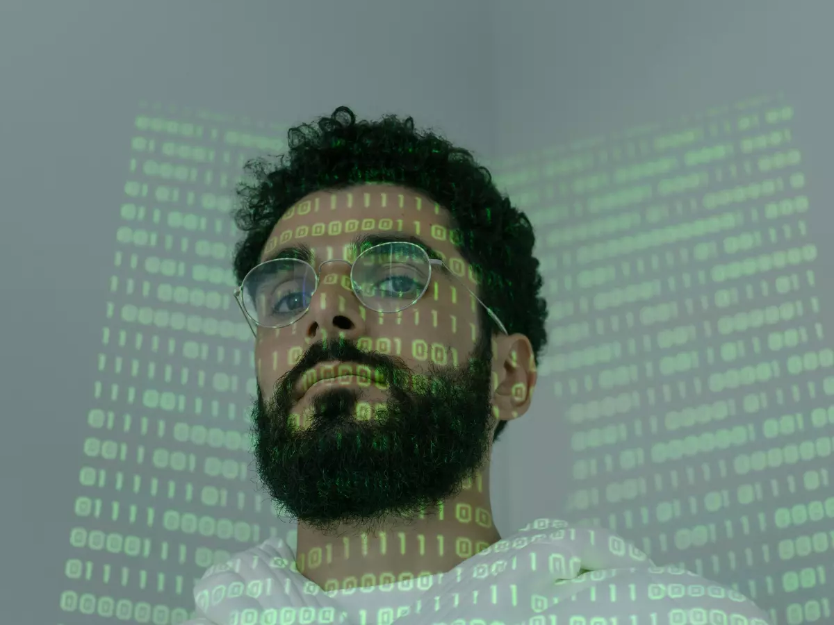 A man with a beard and glasses is looking up, and his face is covered with binary code.