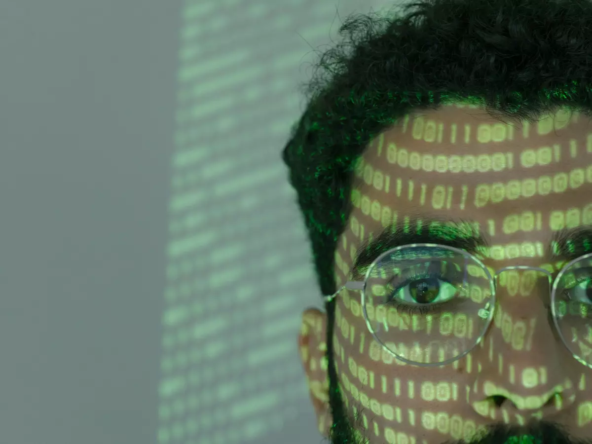 A close-up shot of a man wearing glasses with green code overlaying his face. 