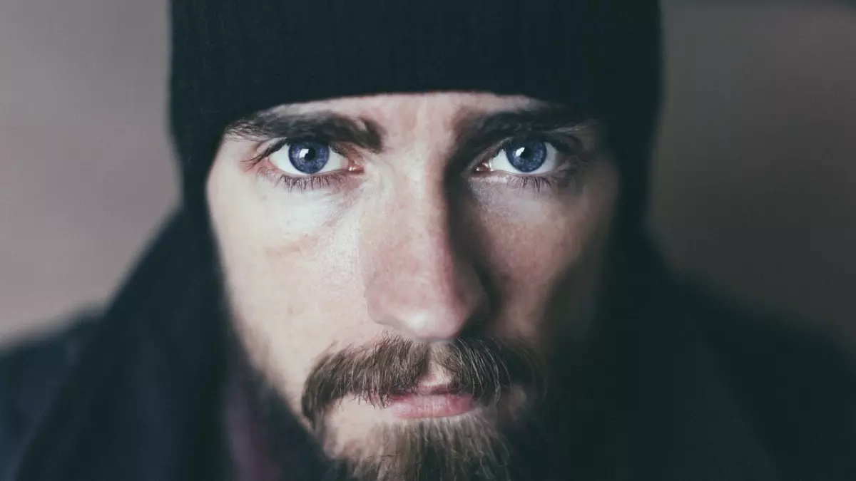 Close-up portrait of a man with a beard and a beanie, looking directly at the camera with a serious expression.