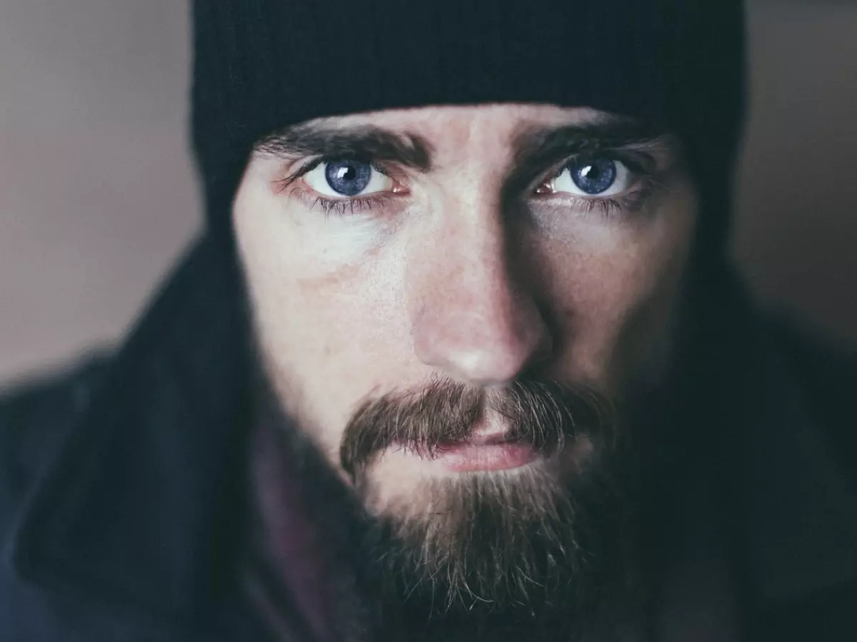 Close-up portrait of a man with a beard and a beanie, looking directly at the camera with a serious expression.