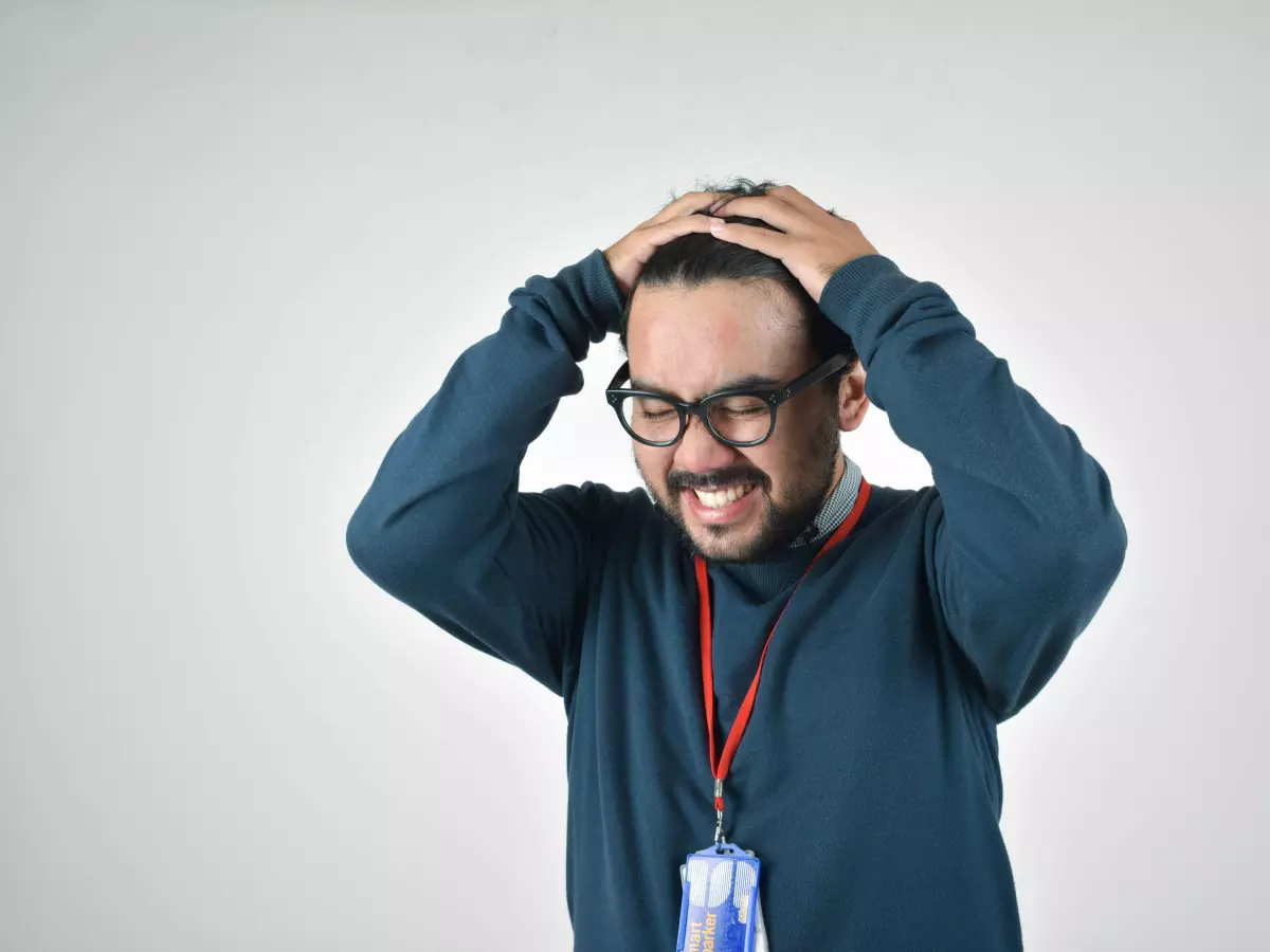 A man with a beard is holding his head in his hands. He looks distressed and frustrated.