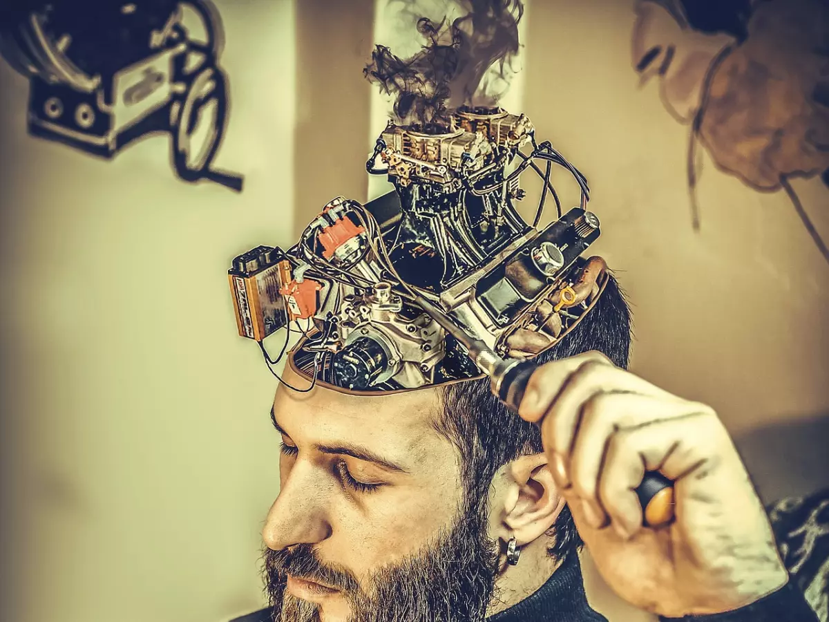 A man with a beard, wearing a sweater, has a large steampunk contraption connected to his open skull. The device has metal gears, wires, and pipes, creating a dramatic visualization of a brain implant.