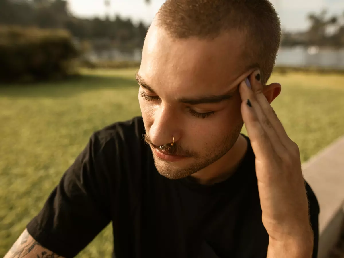 A man is sitting on a couch and holding his head in his hand, looking down.