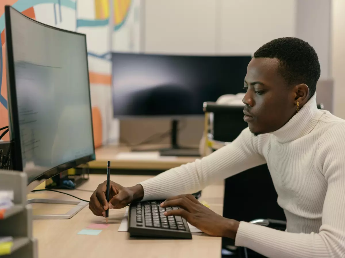 A man sitting at a desk in front of a computer with a pen in his hand looking at the screen