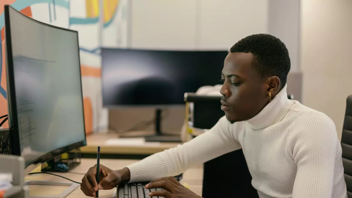 A man sitting at a desk in front of a computer with a pen in his hand looking at the screen