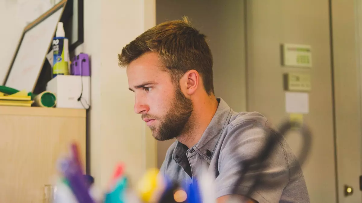 Person working on a laptop with an hourglass in the foreground