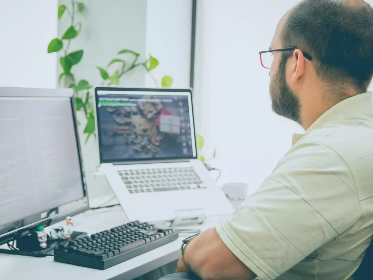 A man working on a laptop at a desk in front of a second monitor.