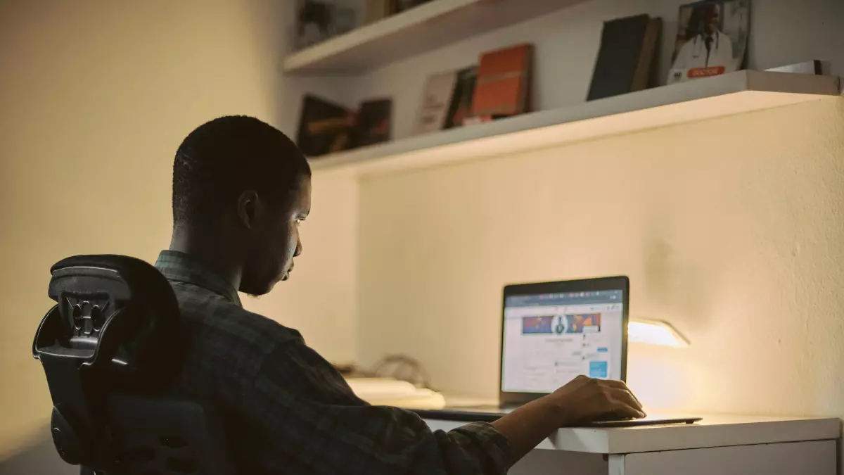 A man sitting at a desk working on a laptop with a frustrated look.