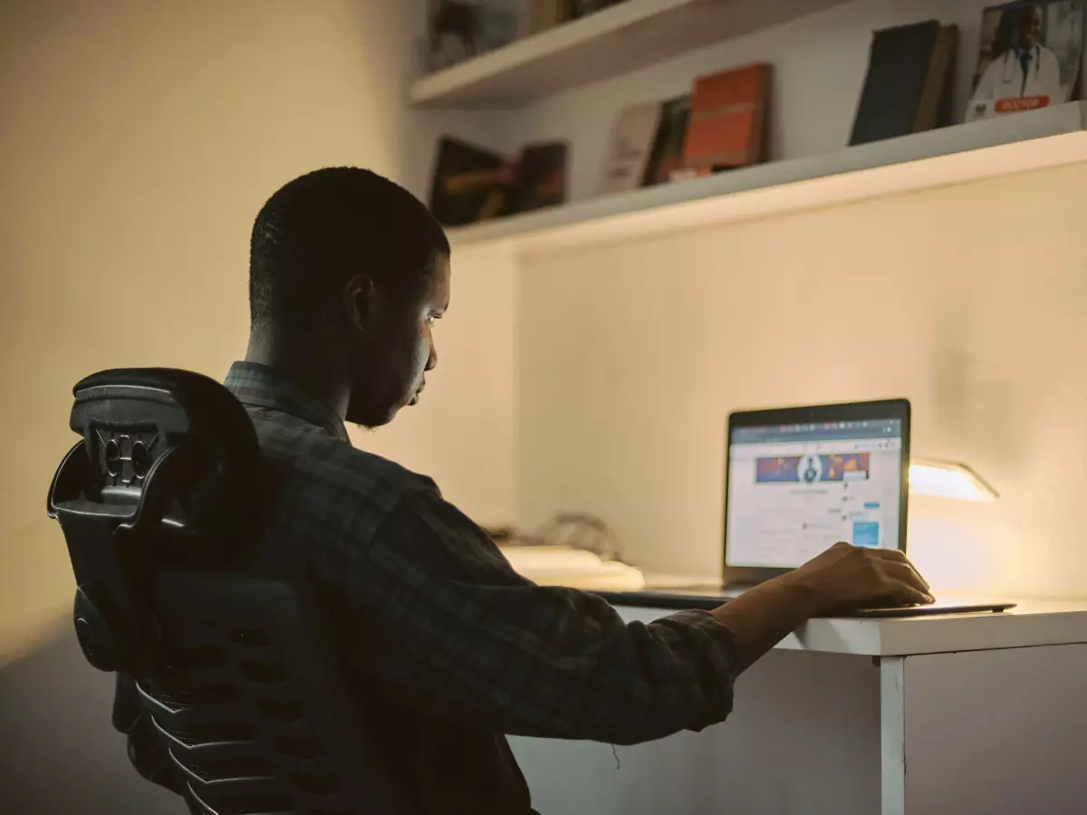 A man sitting at a desk working on a laptop with a frustrated look.