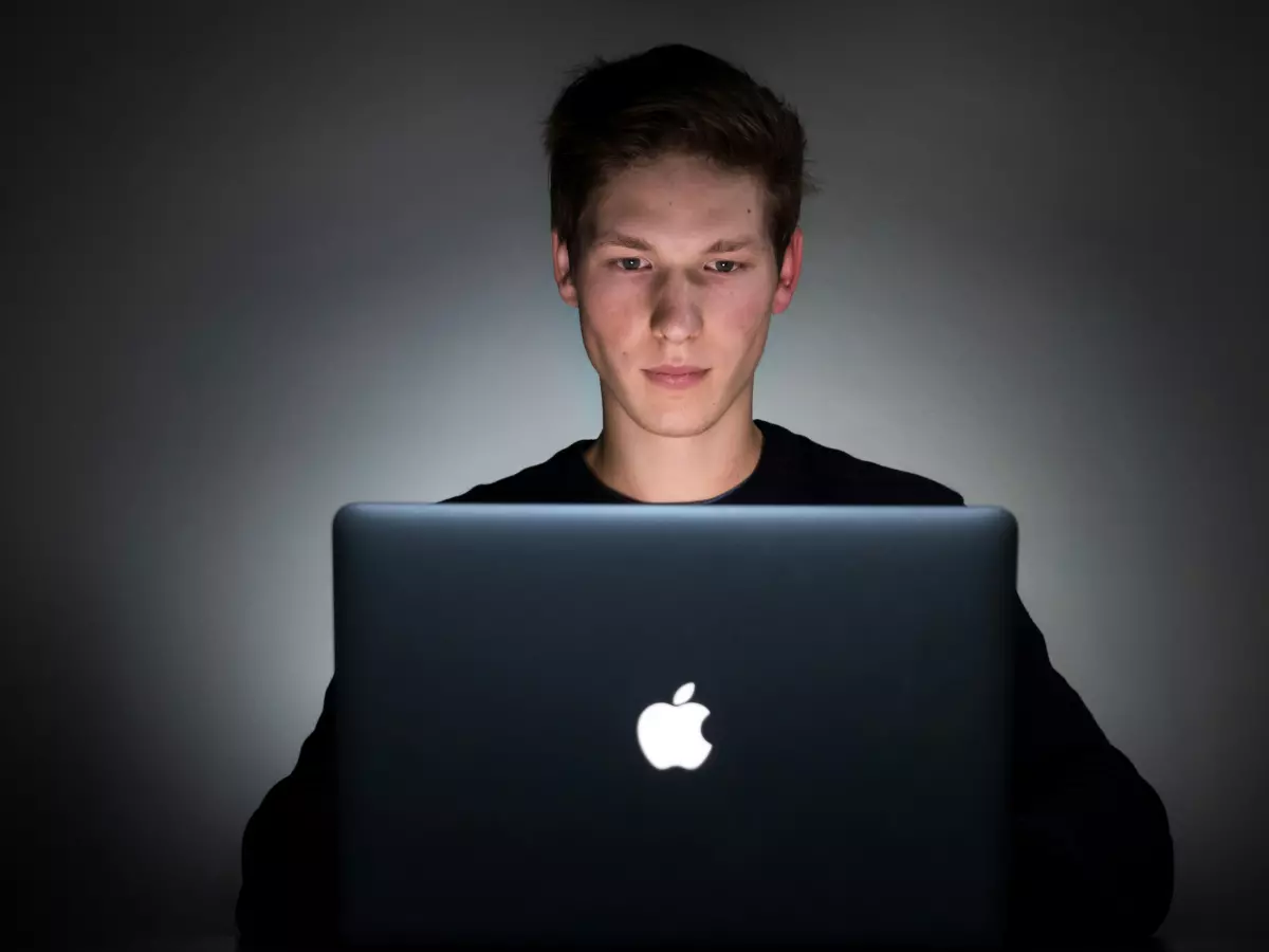 A man is sitting in a dark room and working on a laptop.