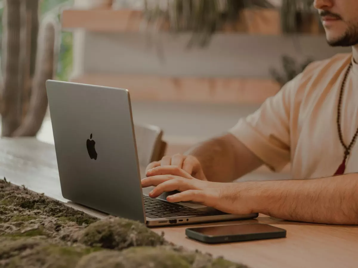 A person typing on a laptop at a table, with a phone next to it.