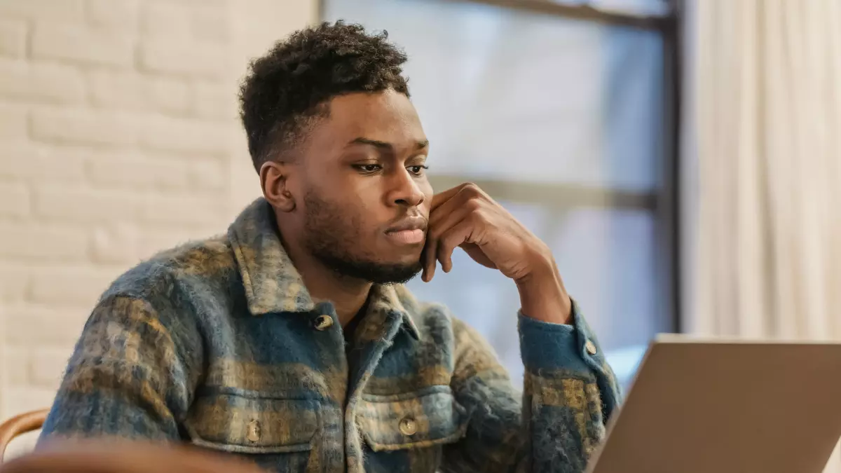 A man with a plaid shirt works on his laptop in a home office.