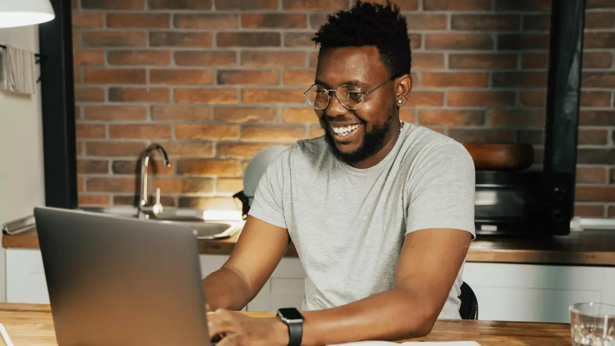 A man smiling and typing on his laptop.