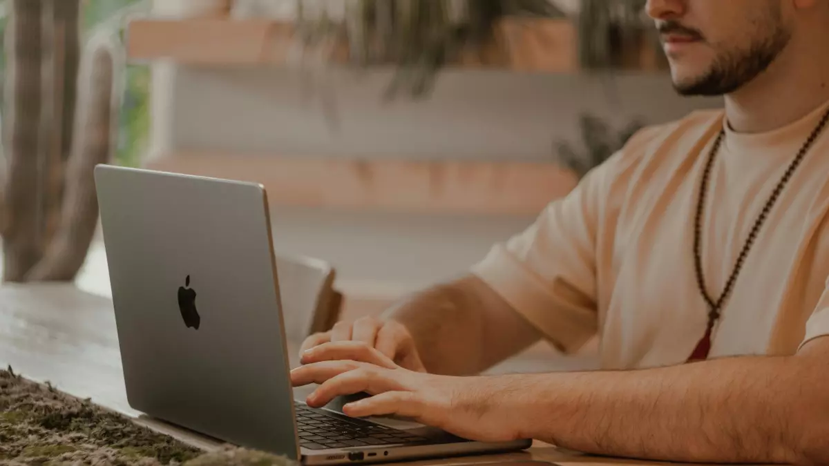 A person typing on a laptop at a table, with a phone next to it.