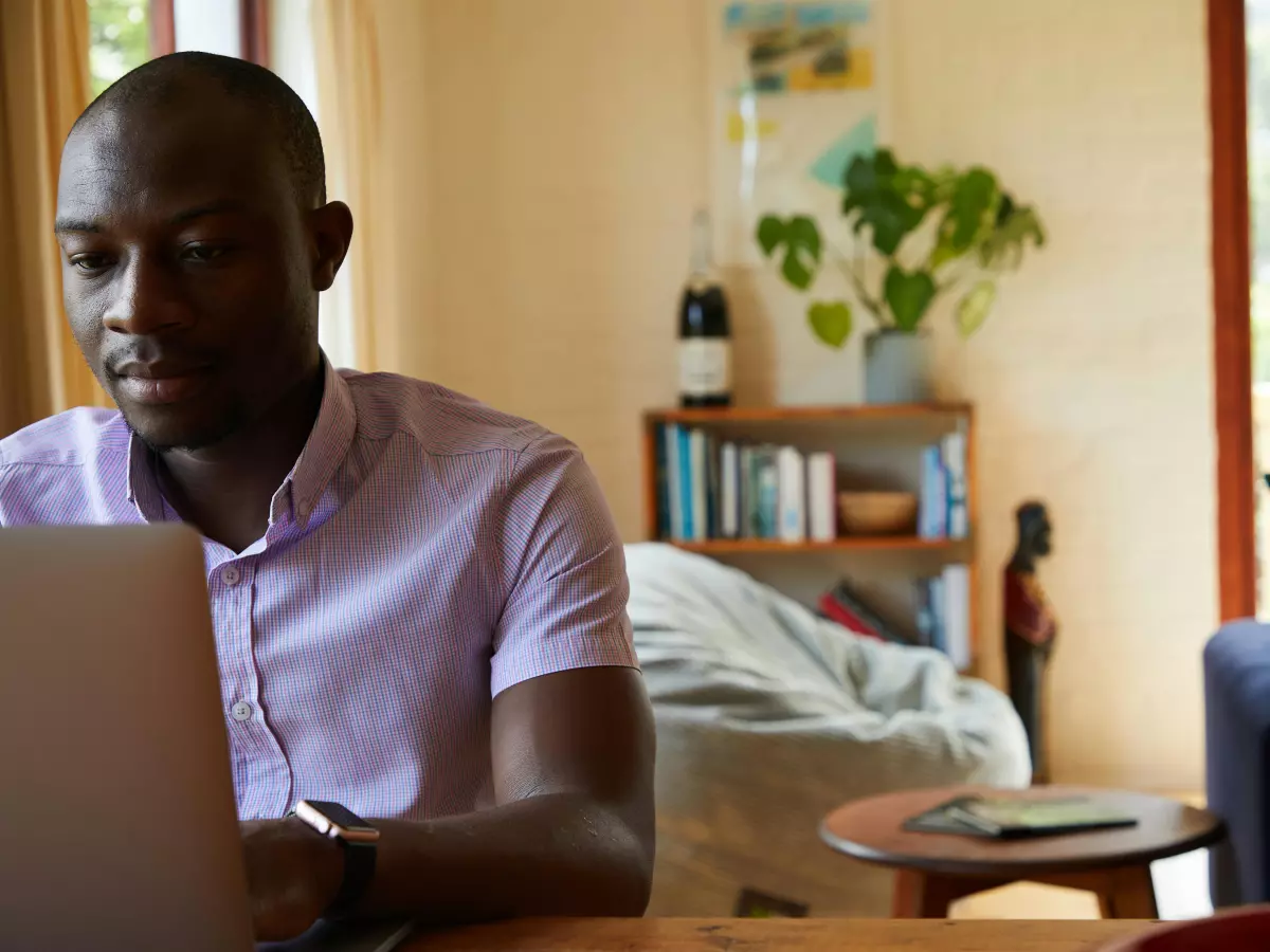 A man working on a laptop in a living room with a bean bag chair in the background.