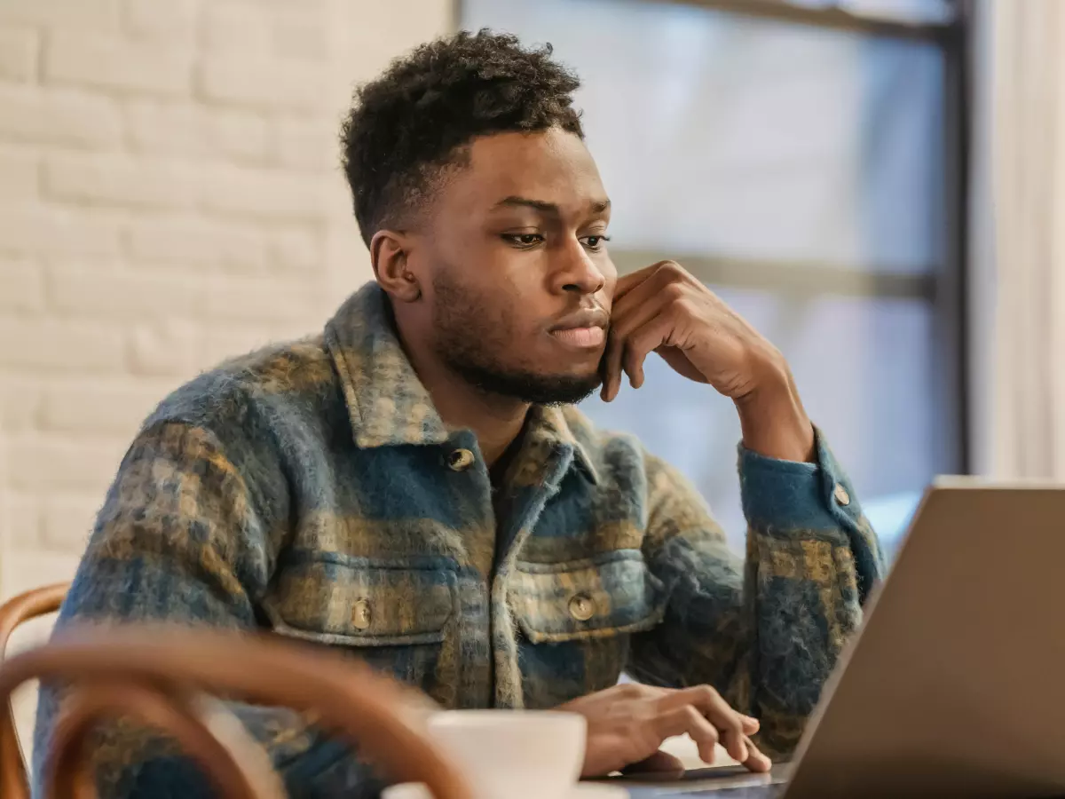 A man with a plaid shirt works on his laptop in a home office.