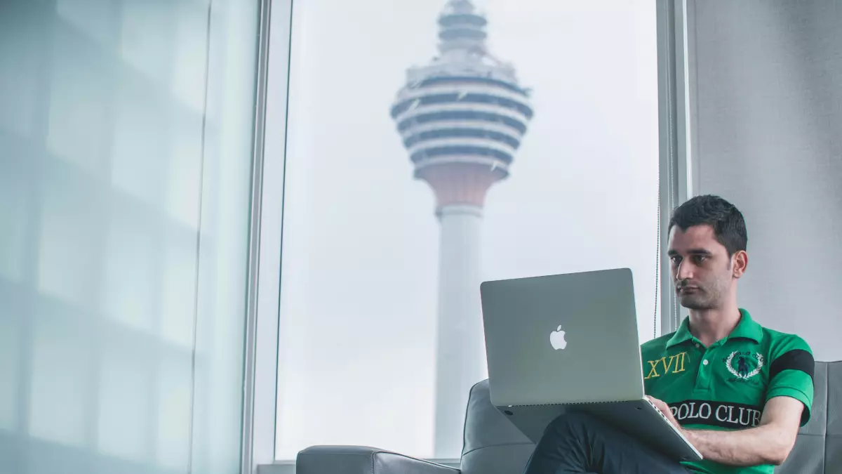 A man working on a MacBook in a modern office space, with a view of a city skyline through the window