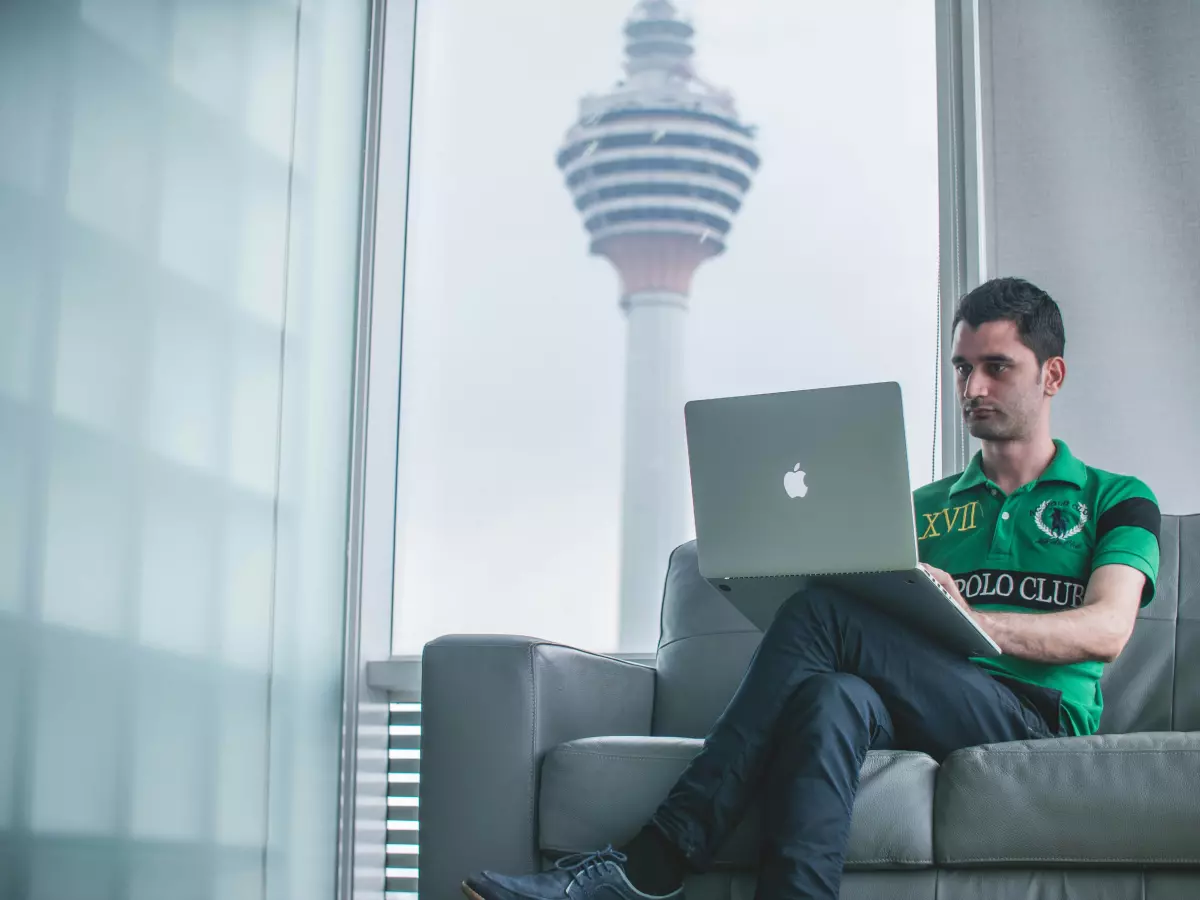 A man working on a MacBook in a modern office space, with a view of a city skyline through the window