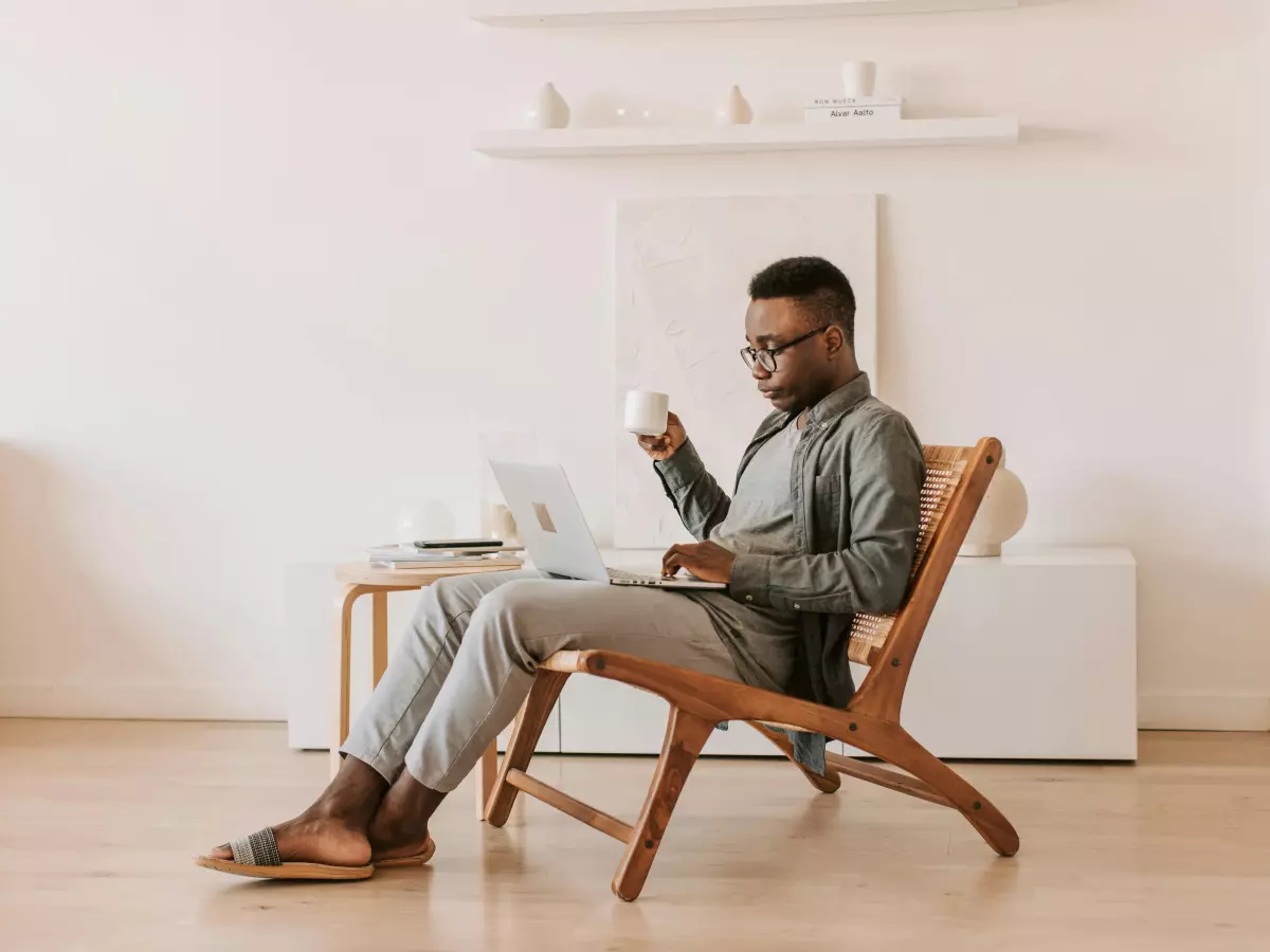 A man sitting in a chair, using a laptop, looking focused and engaged.