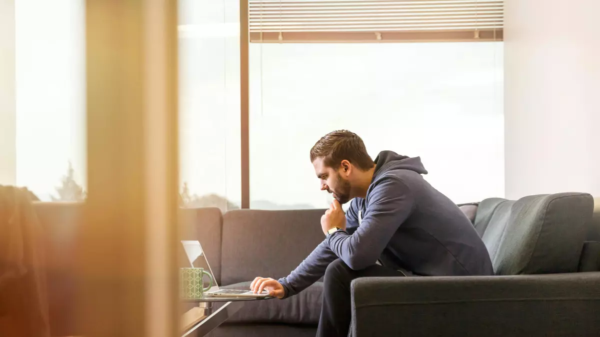 A man sitting on a couch using a laptop, with a focused expression.