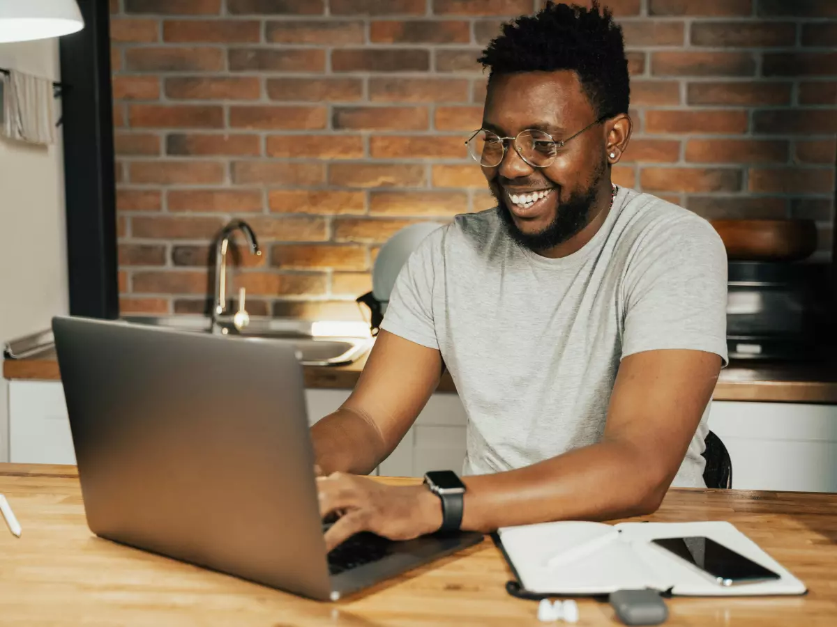 A young man is sitting at a table, looking at a laptop screen and smiling, 