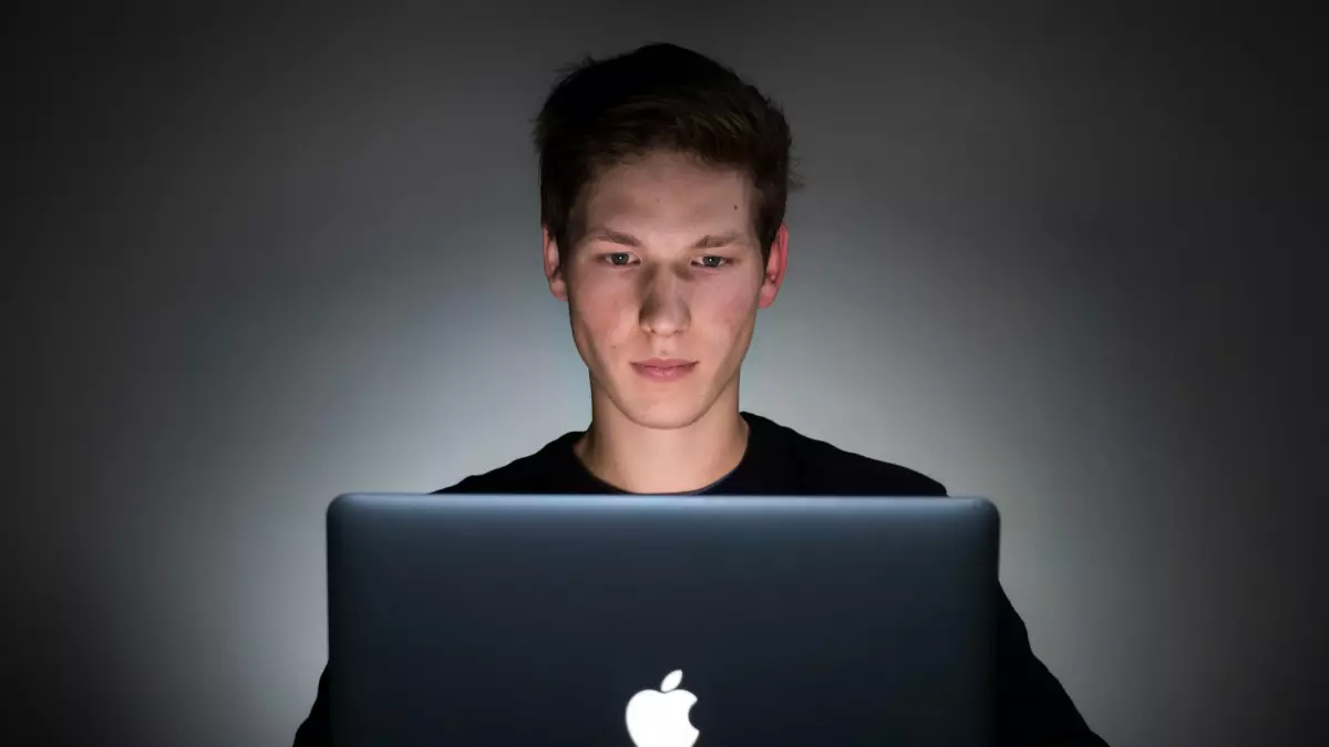 A man is sitting in a dark room and working on a laptop.