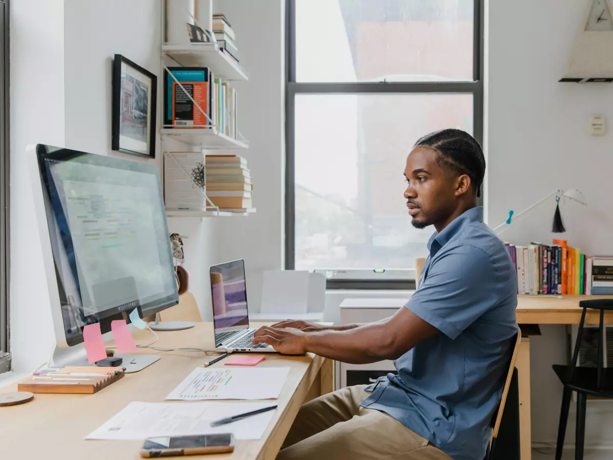 A man sits at a desk in front of a computer. He is looking at the screen and typing on the keyboard.