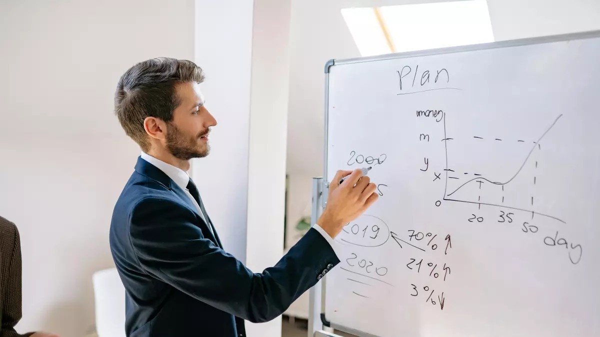 A man in a suit is writing on a whiteboard with a diagram on it. 