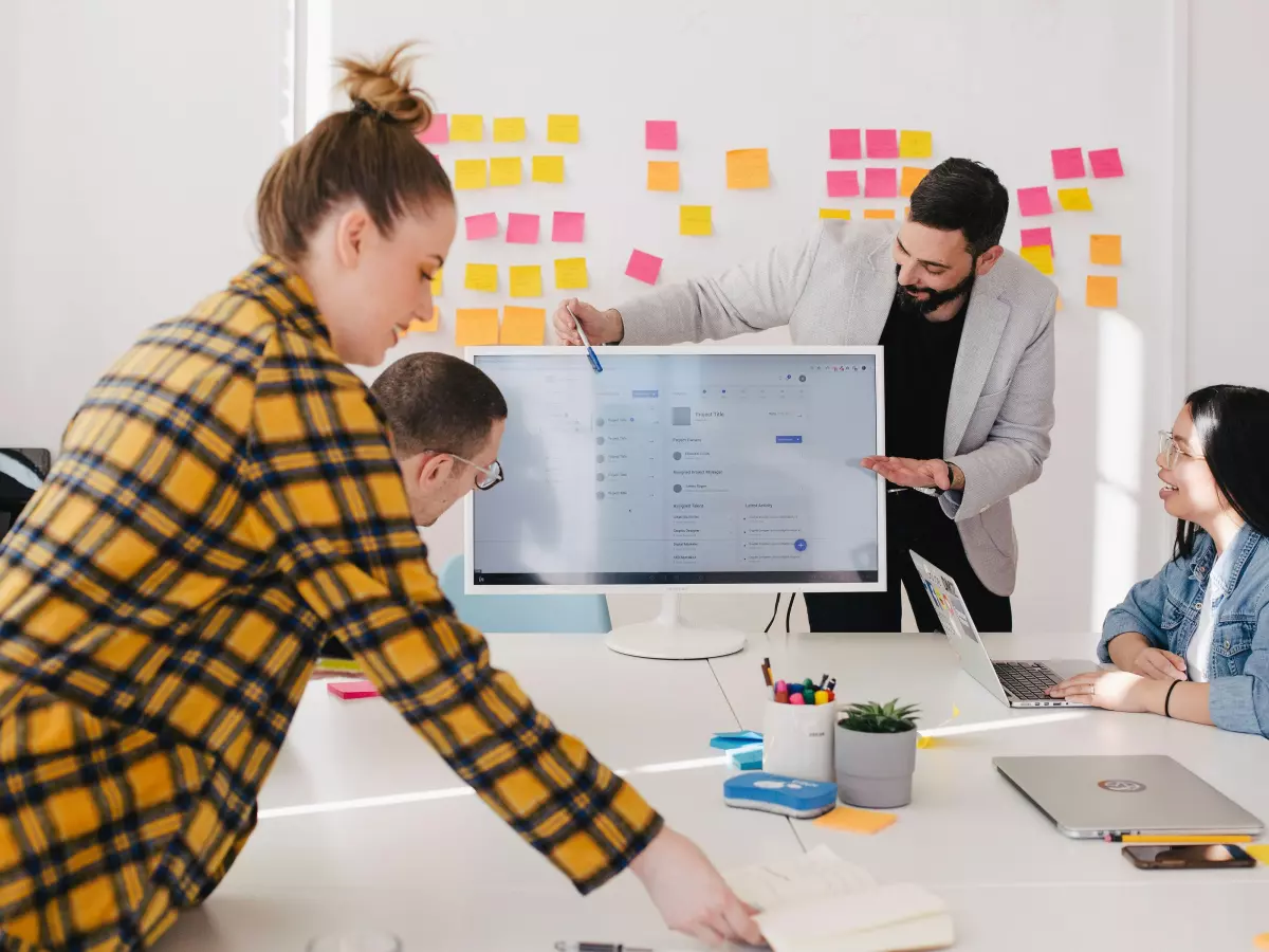 A group of four people in a bright office space, gathered around a table with a large monitor, presenting a strategy for a successful business. 