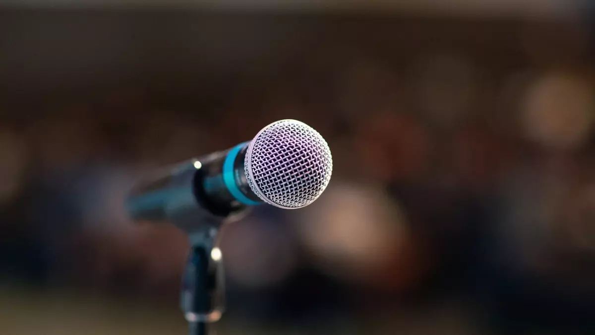 A close-up shot of a microphone on a stand in front of a blurry background of an audience.