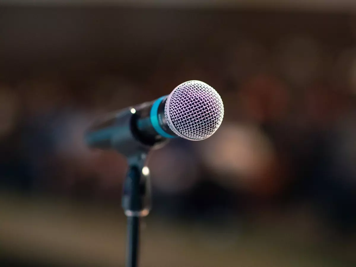 A close-up shot of a microphone on a stand in front of a blurry background of an audience.