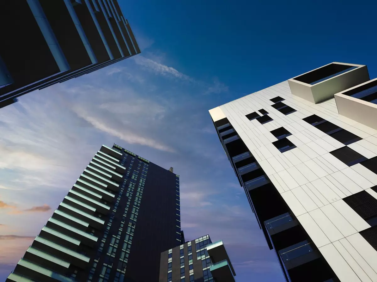 Three high-rise buildings in a modern architectural style, seen from a low angle against a bright blue sky.