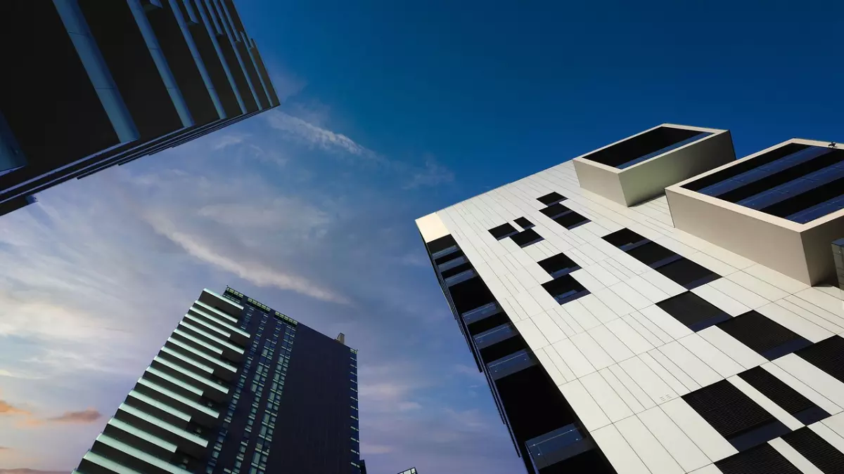 Three high-rise buildings in a modern architectural style, seen from a low angle against a bright blue sky.