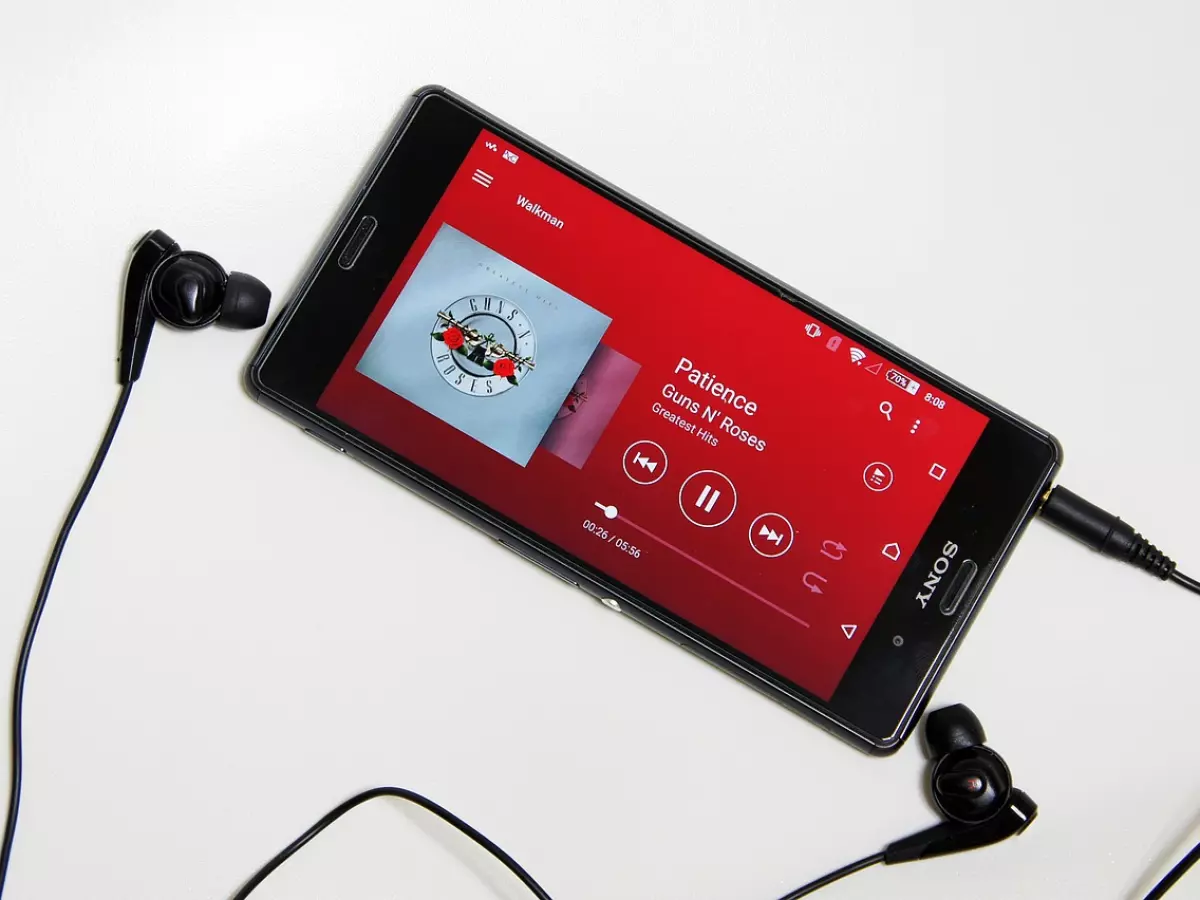 A smartphone with a red screen playing music with black headphones on each side