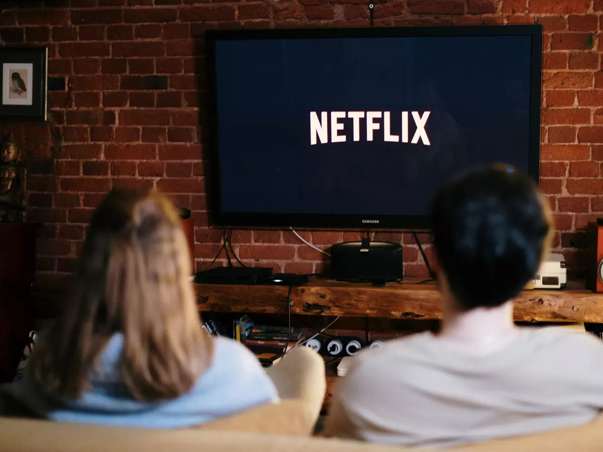 A couple sitting on a couch in front of a TV displaying the Netflix logo.