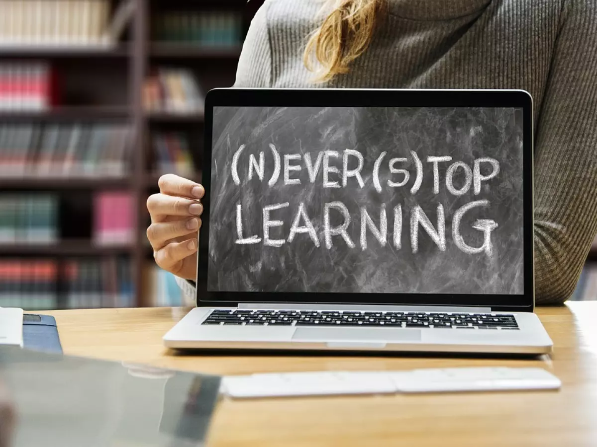 A person holding a laptop with a handwritten message on the screen that reads 'Never Stop Learning'.