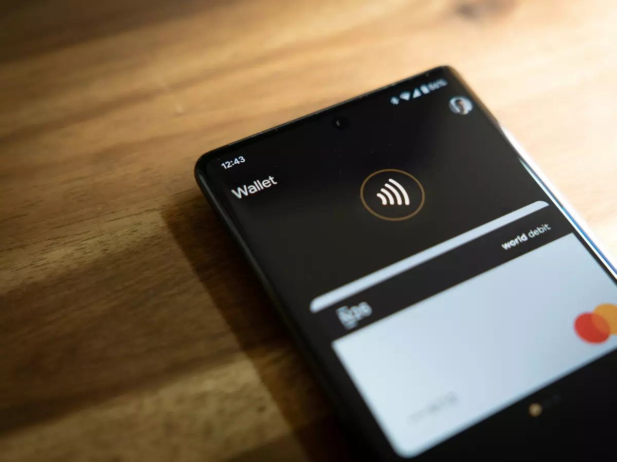 A close-up of a smartphone screen displaying the Google Wallet app. The phone is lying on a wooden surface, showcasing a dark background.