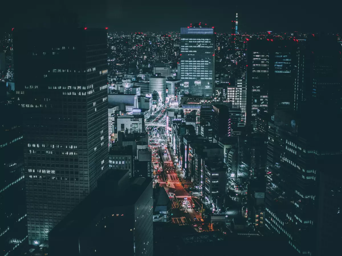 A high-angle, night-time view of a sprawling metropolis with brightly lit buildings and roads.