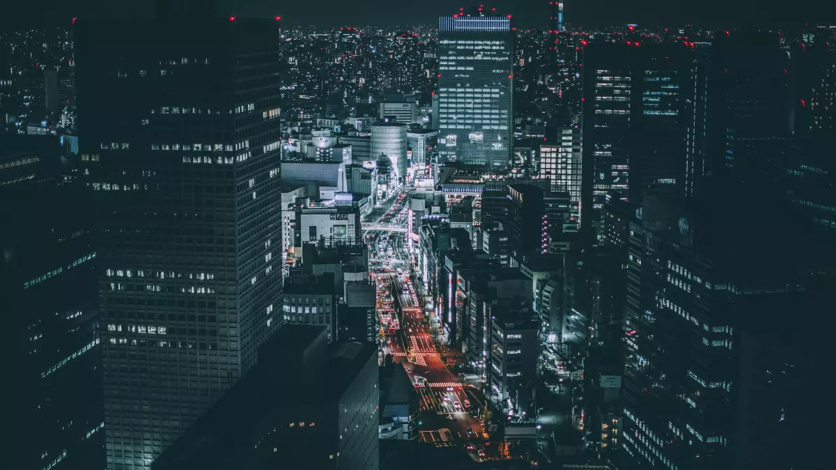 A high-angle, night-time view of a sprawling metropolis with brightly lit buildings and roads.