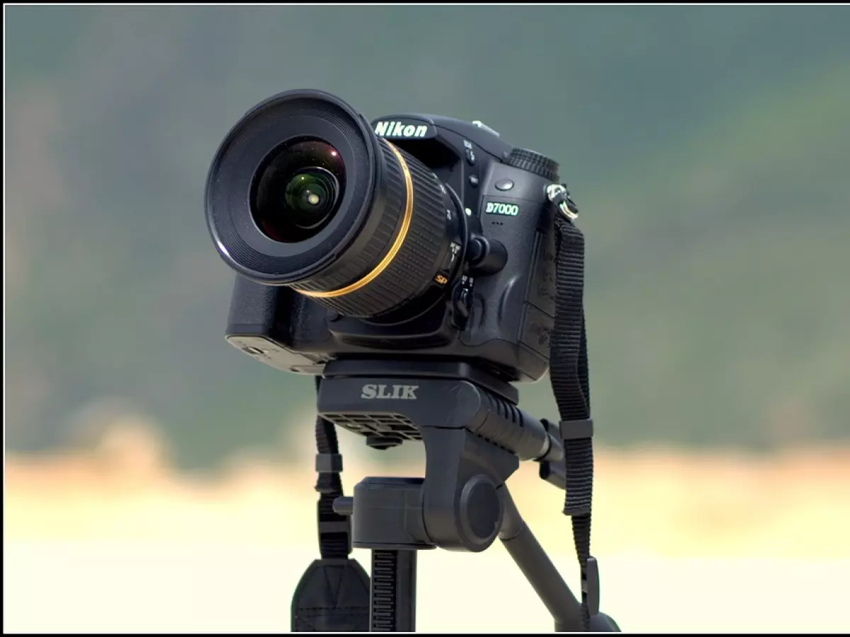 A black DSLR camera mounted on a tripod, the camera is in focus and the background is blurred out. 