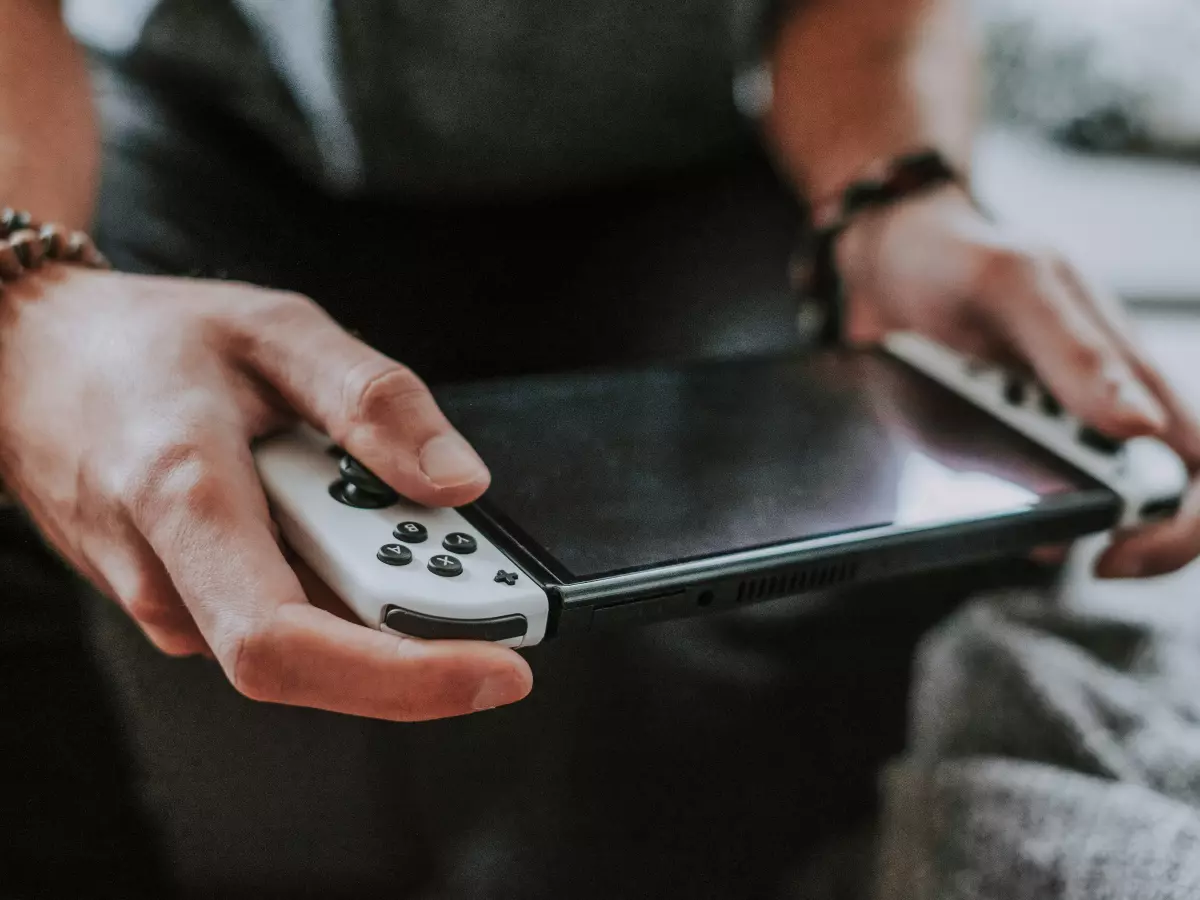 A close-up shot of a Nintendo Switch console being held in someone's hands. The buttons and screen are visible. 