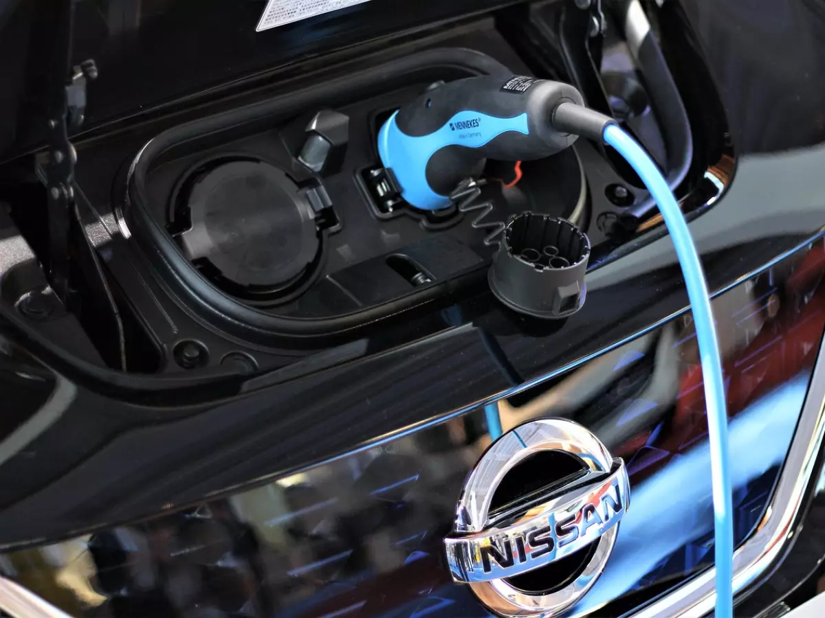 A close-up image of a Nissan Leaf EV's charging port with the charging cable plugged in, revealing the Nissan emblem.