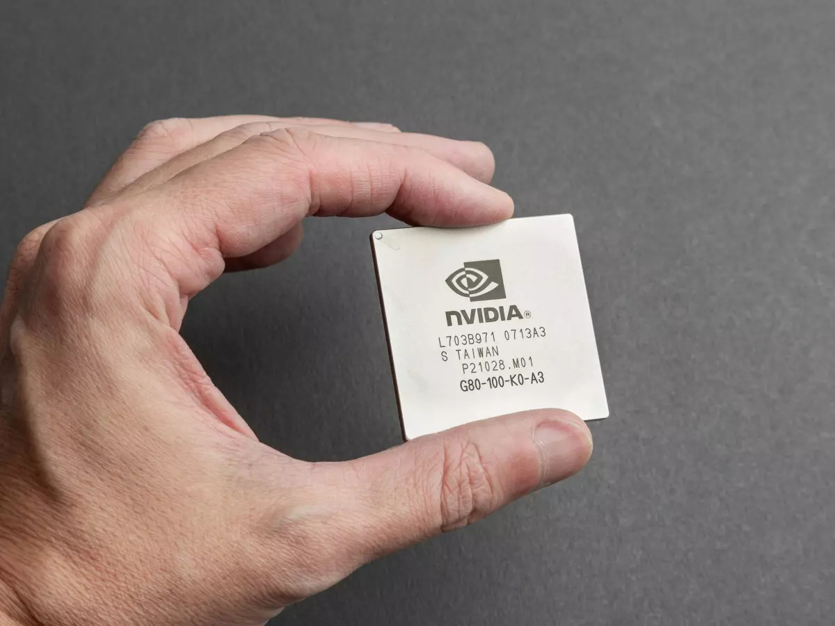 A hand holding a small, square Nvidia chip with the Nvidia logo visible.