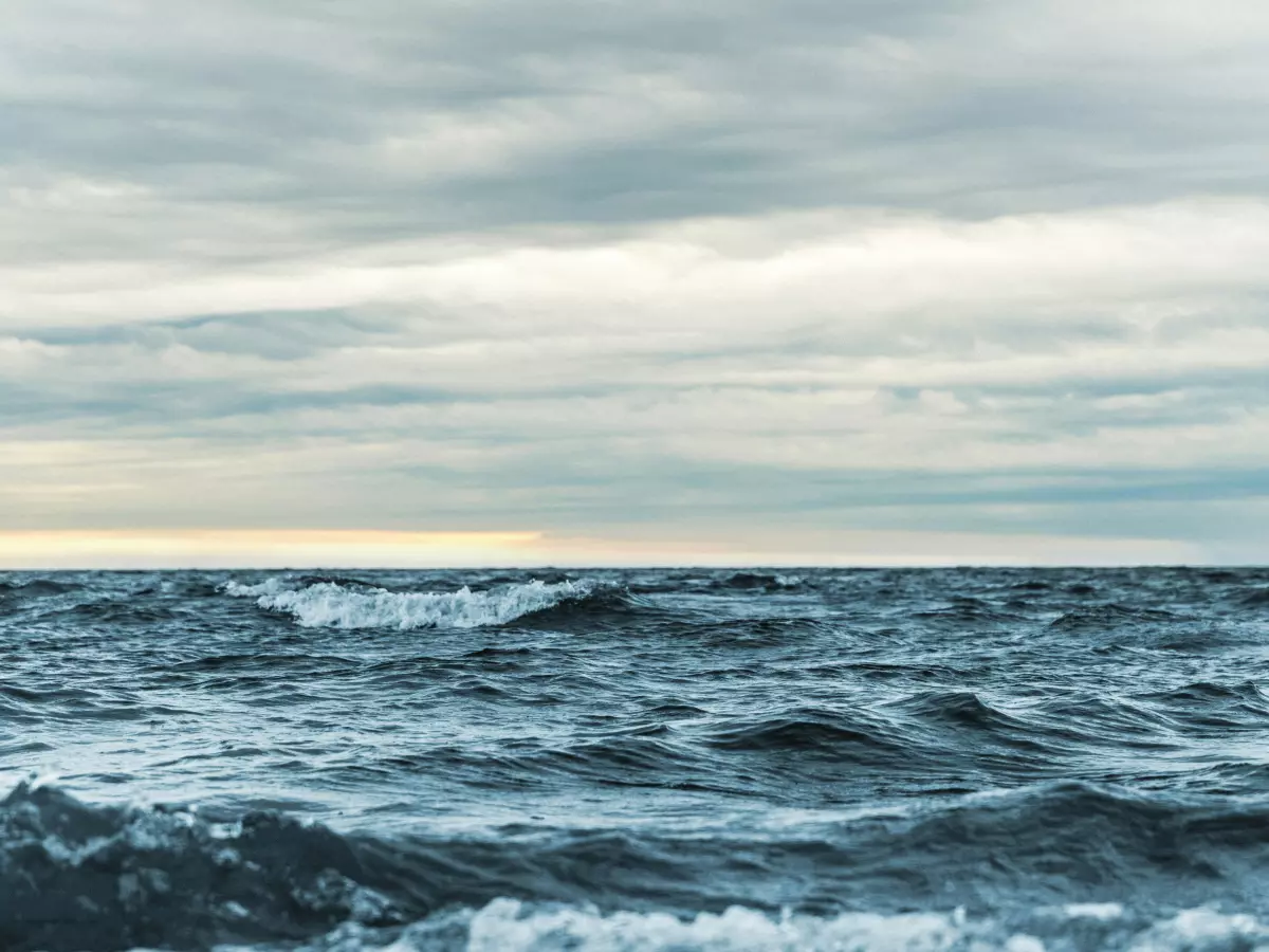 A wide view of the ocean with waves and a cloudy sky.