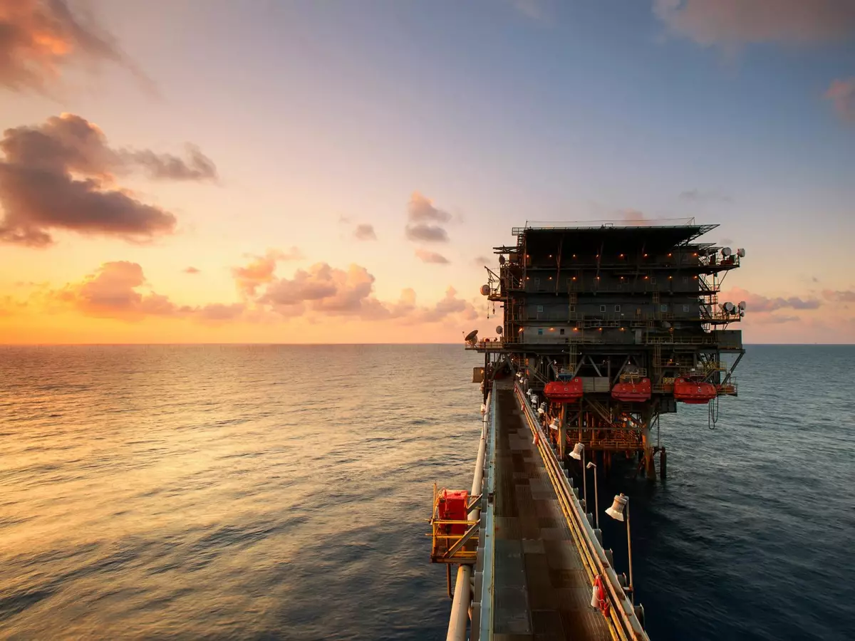 An oil rig platform standing tall on the vast ocean under a dramatic sunset sky. 