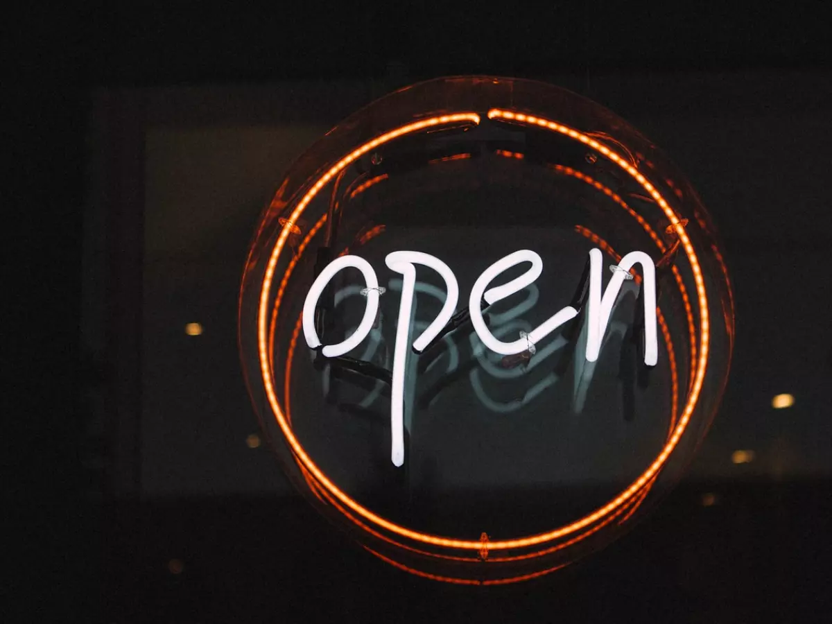 A neon sign in the shape of a circle with the word 'open' in white inside the circle. The background is blurred. 